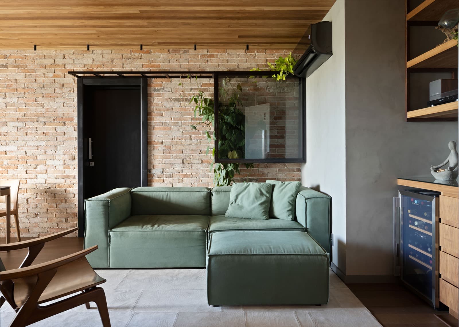 Sala de estar com sofá verde diante da parede de tijolo aparente